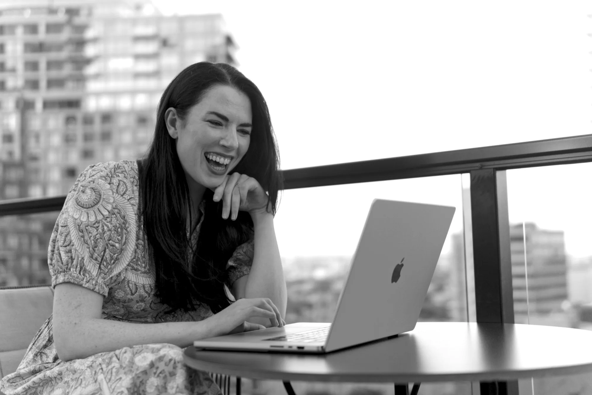 Black-and-white portrait of Sarah-Jayne laughing beside a laptop